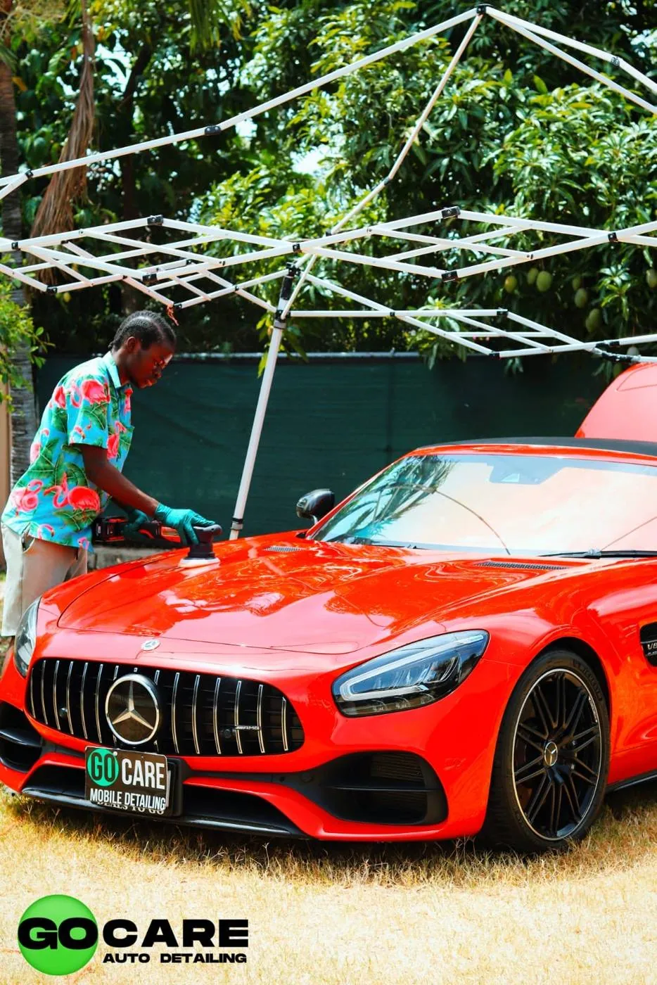 Go Care technician machine polishing a red Mercedes-AMG under a canopy